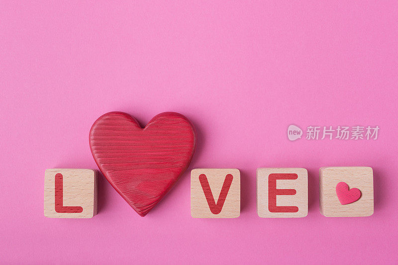 Word Love made of wooden blocks and decorative valentines heart. Pink background with copy space. Valentineâs day conceptual greeting